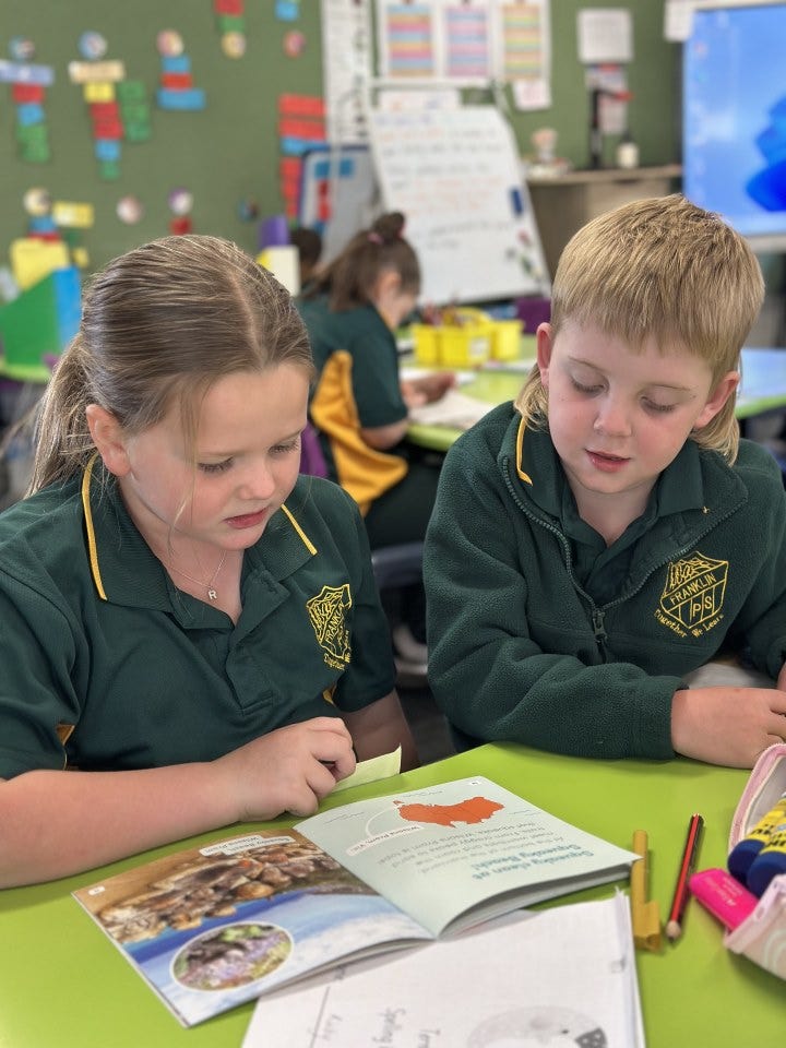 Two students buddy reading at a desk in the classroom.