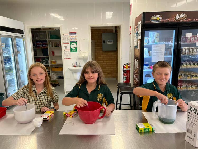 Three students measuring ingredients and cooking in the school canteen.