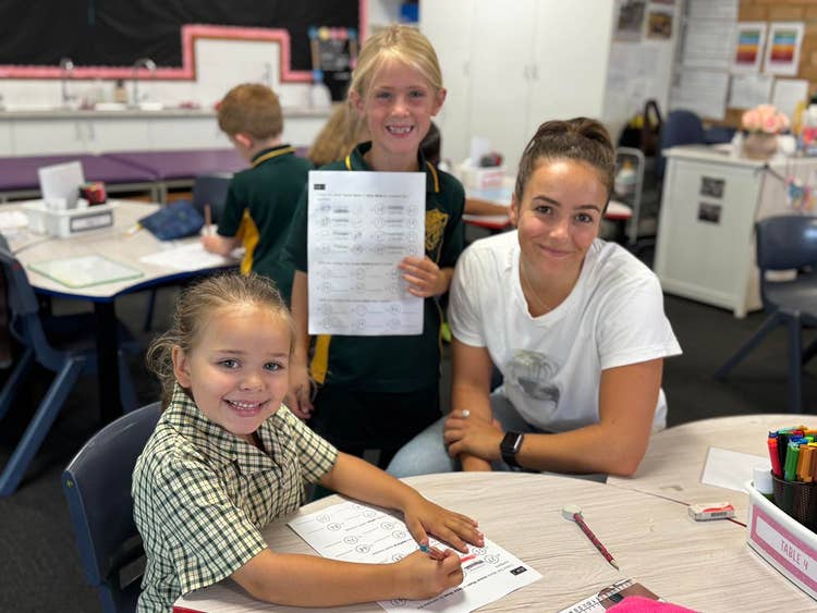 SLSO working with two students at a desk in the classroom.