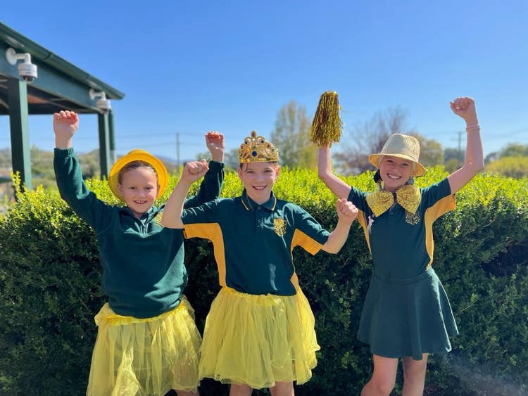 Three students wearing yellow accessories fist pumping the air for R U OK? Day.