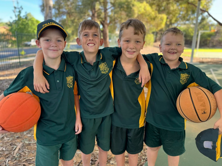Four boys on the basketball court holding basketballs with arms around each other.